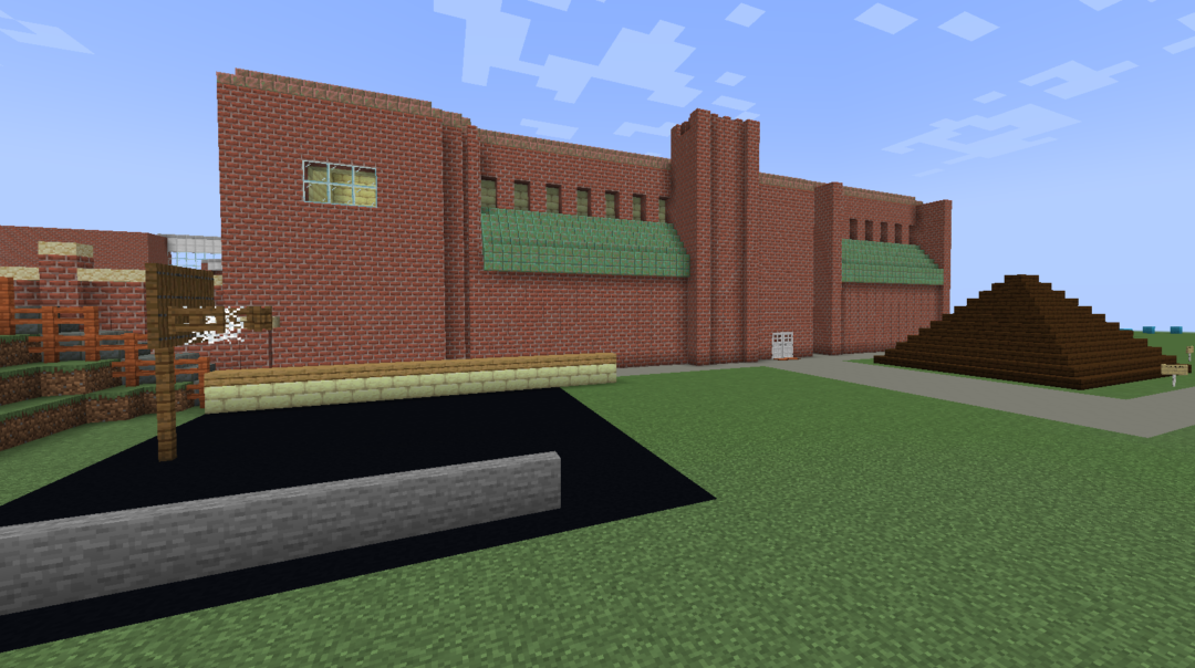 A minecraft model of Jimmy Lee/Oxford Rec center, circa 1971. It is a brick building with green copper accents. In front of it is a basketball court and a wooden climbing pyramid.